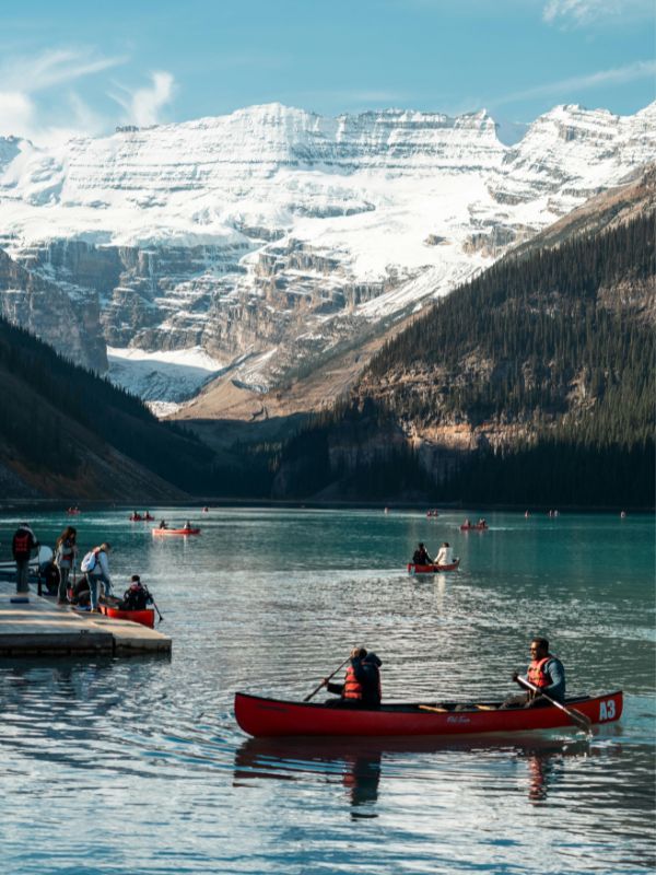 The bright blue Lake Louise with a red canoe floating on it and surrounded by snow capped peaks.